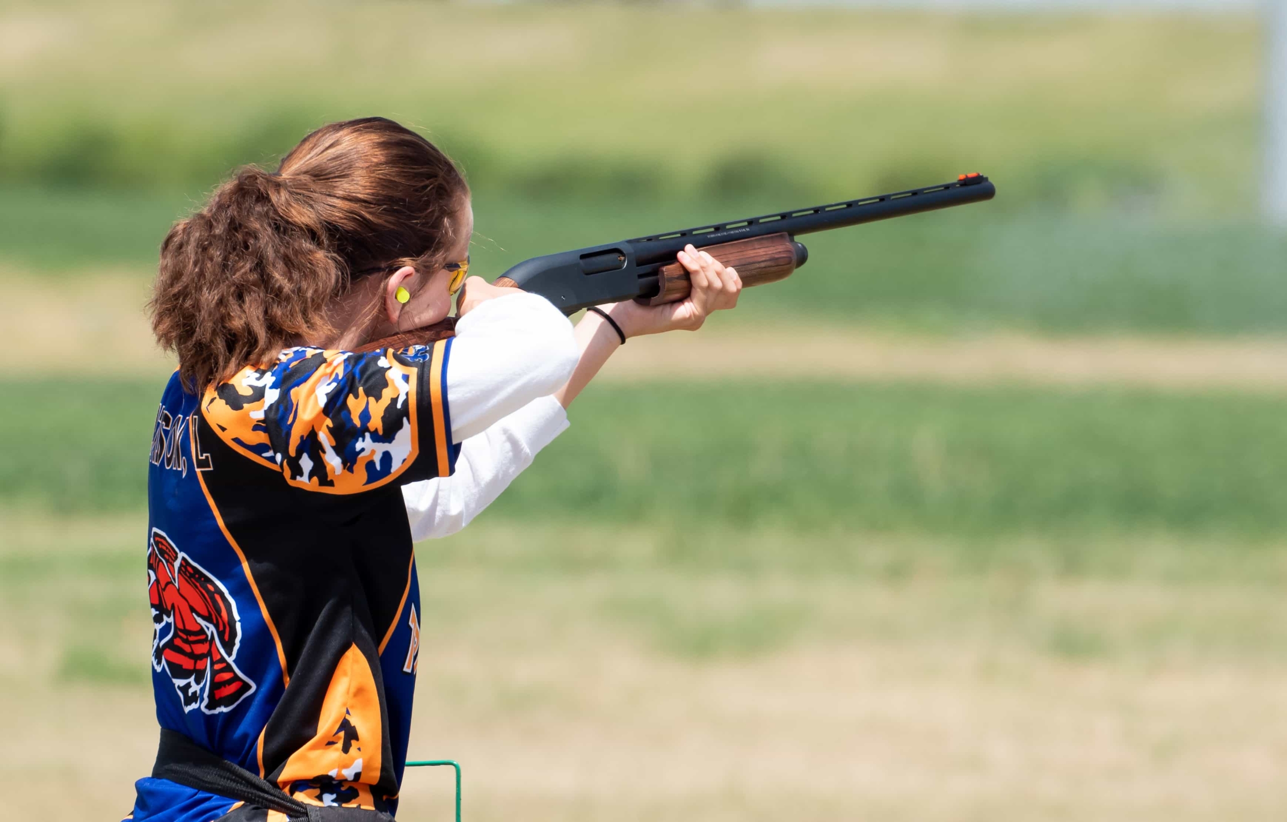 A girl is shooting a gun in an open field.