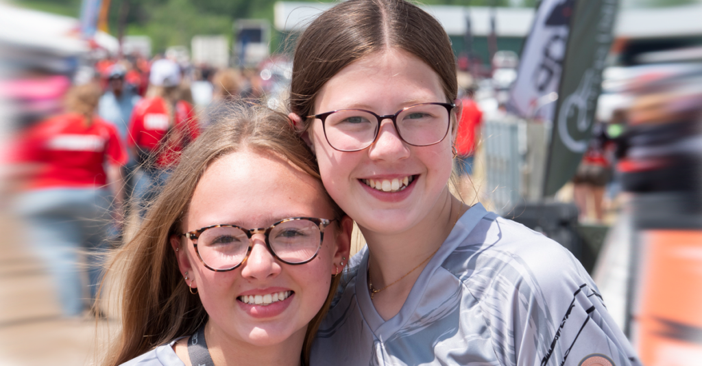 Two girls in glasses smile for the camera at an event.